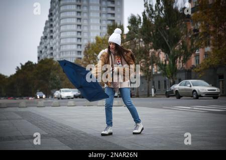 Femme avec parapluie bleu pris dans la rafale de vent dans la rue Banque D'Images