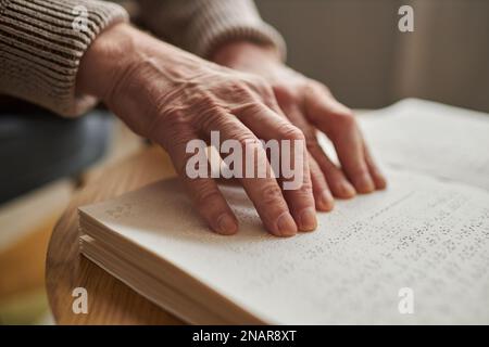 Gros plan d'un homme âgé aveugle utilisant ses mains pour lire un livre à table Banque D'Images