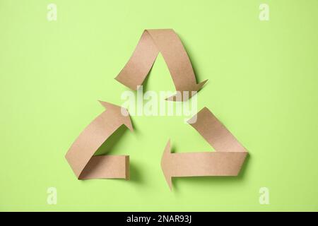 Symbole de recyclage coupé en papier sur fond vert, vue de dessus Banque D'Images