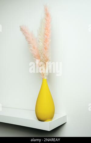 image verticale d'une étagère blanche isolée avec un petit vase en porcelaine jaune avec des plantes séchées décoratives et un mur peint blanc uni Banque D'Images