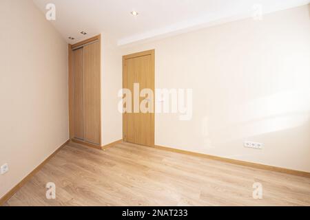chambre vide d'une maison avec parquet stratifié et petite armoire avec portes coulissantes en bois dans un coin Banque D'Images