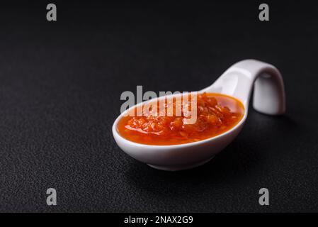 Sauce adjika rouge ou ketchup aux épices et aux herbes sur fond de béton foncé Banque D'Images