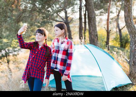 Allons camper. Camping familial. Atteindre le lieu de destination. Adolescentes gaies parlant sur un appel vidéo, regardant l'écran du téléphone au milieu de Banque D'Images