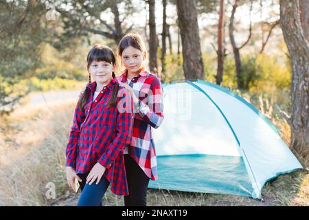 Allons camper. Camping familial. Atteindre le lieu de destination. Les adolescentes gaies sont debout et regardent la caméra au milieu d'une forêt de pins Banque D'Images