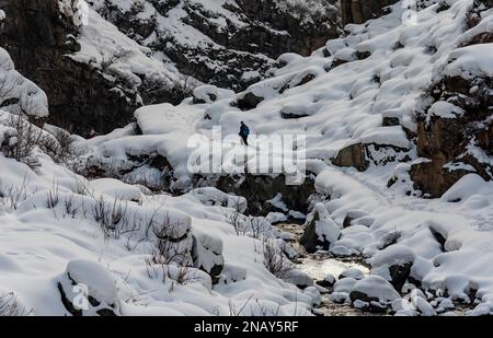 Srinagar, Inde. 13th févr. 2023. Un homme marche le long d'un sentier couvert de neige à côté d'un ruisseau gelé pendant une journée ensoleillée dans la banlieue de Srinagar. Crédit : SOPA Images Limited/Alamy Live News Banque D'Images