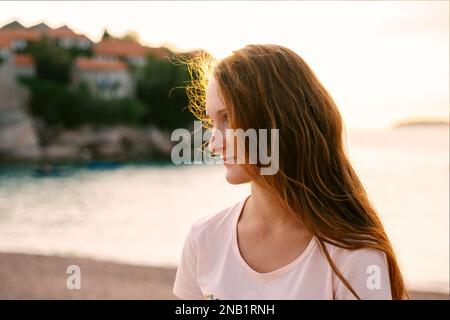 Vue latérale d'un portrait de femme joyeuse à tête rouge sur la plage au coucher du soleil, photo prise à Sveti Stefan Montenegro Banque D'Images