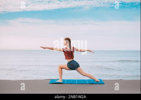 Active Sport redhead femme faisant du yoga sur la plage au Monténégro vue latérale, Femme est dans les vêtements de sport à la plage de la mer Adriatique Banque D'Images