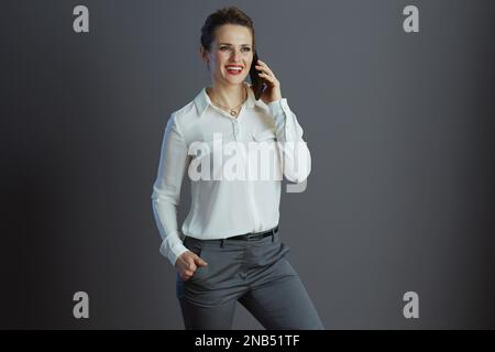 heureuse élégante femme employée dans un chemisier blanc parlant sur un téléphone portable sur fond gris. Banque D'Images