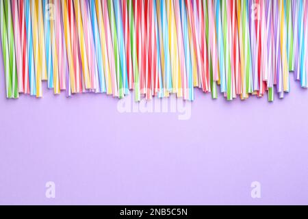 Pailles à boire en plastique coloré sur fond violet, plat. Espace pour le texte Banque D'Images