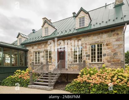 Arrière de l'ancienne maison en pierre de champ de style chalet Canadiana de 1826 avec toit en tôle de couture debout verte, solarium et arbustes Hydrangea, plantes Hosta. Banque D'Images