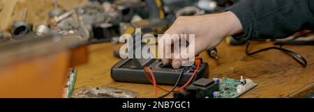 Gros plan des mains d'électricien vérifie la tension électrique sur la carte de circuit imprimé à l'aide d'un dispositif Banque D'Images