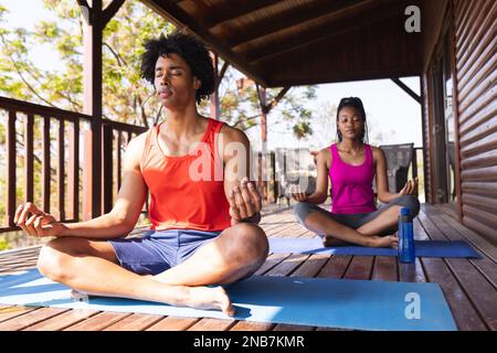 Couple afro-américain passant du temps dans une cabine de bûche pratiquant le yoga sur des tapis de yoga. Chalet, nature et style de vie. Banque D'Images
