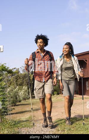 Heureux couple afro-américain marchant avec des bâtons de randonnée dans la campagne le jour ensoleillé. Concept de pays, de nature et de style de vie. Banque D'Images