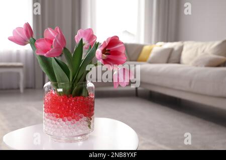 Différentes couleurs de remplissage et tulipes dans vase en verre sur table blanche à la maison, espace pour le texte. Perles d'eau Banque D'Images