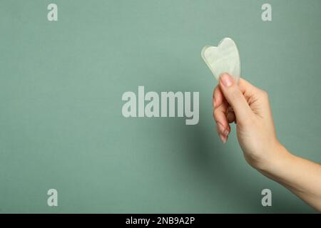 Femme avec l'outil Jade gua sha sur fond gris vert, gros plan. Espace pour le texte Banque D'Images