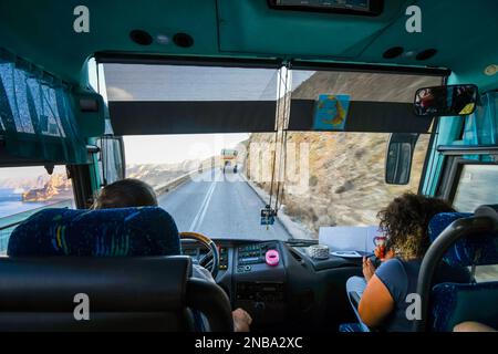 La vue de l'intérieur d'un bus de visite le long de la route sinueuse de colline d'Oia au port de Santorin Grèce, avec la mer et bateau de croisière au loin Banque D'Images