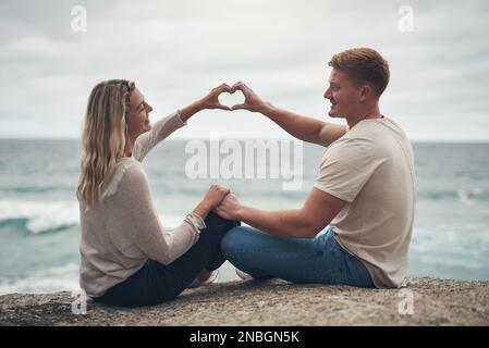Vous m'avez enseigné le vrai sens de l'amour. un couple formant un coeur avec leurs mains tout en étant assis sur la plage. Banque D'Images