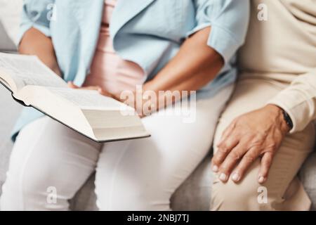 Mains, bible et prier avec un couple senior lisant un livre ensemble dans leur maison pendant la retraite. Jésus, foi ou croyance avec un homme et une femme Banque D'Images