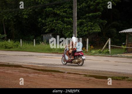 Une femme à moto avec deux enfants dans une campagne à Ko Lanta, Krabi, Thaïlande. 4 décembre 2022. Banque D'Images