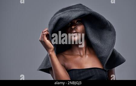 Je garde ma belle peau protégée du soleil. une jeune femme portant un grand chapeau de soleil sur fond gris. Banque D'Images