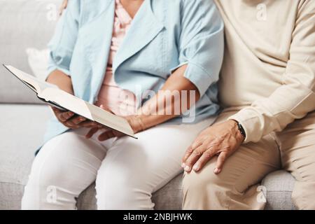 Mains, bible et prier avec un vieux couple lisant un livre ensemble dans la maison pendant la retraite. Jésus, foi ou croyance avec un homme et une femme âgés Banque D'Images