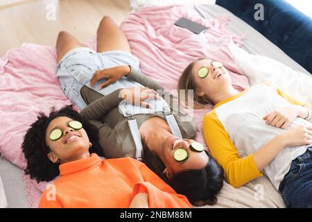 Heureux diverses adolescentes amies allongé sur le lit avec des tranches de concombre sur les yeux. Passer du temps de qualité à la maison concept. Banque D'Images