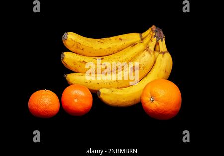 Image de bananes orange et de deux mandarines sur fond noir Banque D'Images