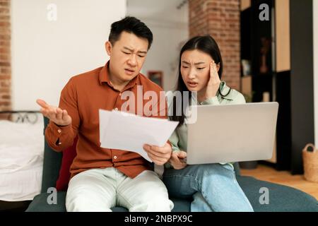 Concept de crise financière. Un couple asiatique vérifie des documents avec un ordinateur portable, souffrant de problèmes avec la gestion du budget familial Banque D'Images