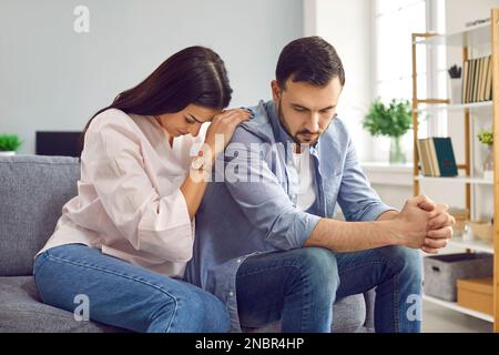 Jeune femme essayant de faire la paix avec mari après querelle assis sur le canapé à la maison. Banque D'Images