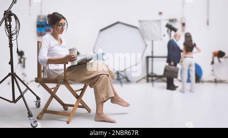 Actrice professionnelle assise sur la chaise du réalisateur et lisant le script, intérieur de studio de film en arrière-plan: Industrie du film et production vidéo Banque D'Images