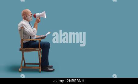 Réalisateur professionnel et confiant assis sur le fauteuil du réalisateur et criant avec un mégaphone, le concept de l'industrie cinématographique Banque D'Images