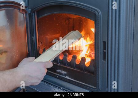 Un homme jette du bois dans la cheminée. Foyer ouvert en fonte avec bois. Banque D'Images