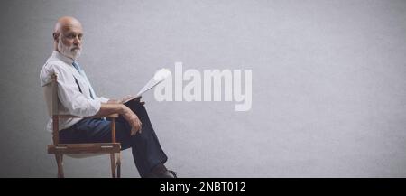 Réalisateur professionnel assis sur la chaise du réalisateur et tenant un scénario, il regarde la caméra Banque D'Images