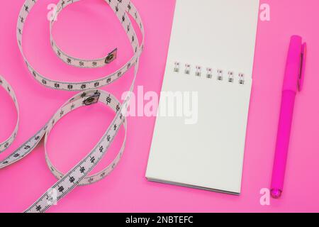Carnet ouvert vierge avec bande au centimètre sur fond rose avec espace pour le texte ou le concept de nourriture d'affaires. Concept sport, alimentation, forme physique, saine alimentation Banque D'Images