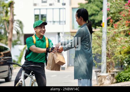 Coursier souriant sur vélo donnant des paquets à la femme Banque D'Images