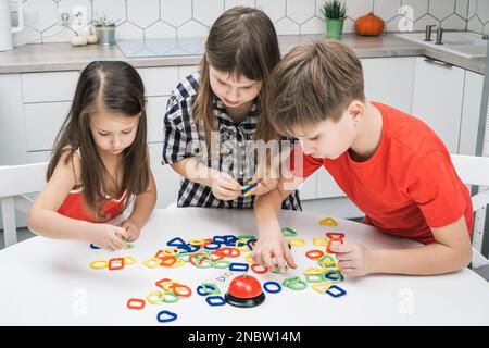 Drôle école enfants jouent jouet constructeur se tenant au-dessus de la table de cuisine et regardant vers le bas, de la vue d'en haut. Garçons et filles collectent des motifs géométriques en plastique Banque D'Images