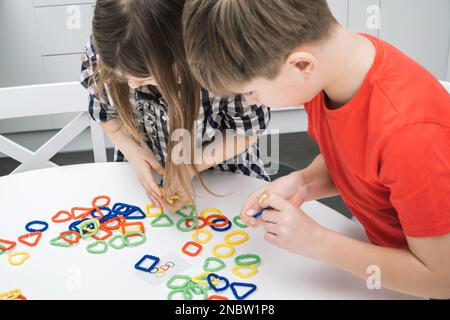 Les enfants de petite école jouent jouet constructeur se tenant au-dessus de la table de cuisine et regardant vers le bas, de la vue d'en haut. Garçon et fille collectent des éléments géométriques en plastique de couleur Banque D'Images