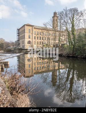 Reflet du bâtiment NHS « New Mill » dans la surface de l'eau au-dessus du déversoir et en dessous du pont Victoria, Saltaire, west yorkshire. Banque D'Images