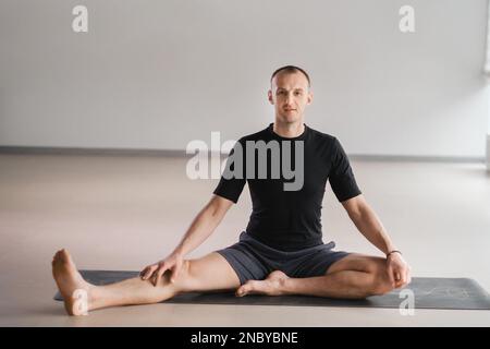 Un homme de construction athlétique fait du yoga dans la salle de gym sur un tapis. Banque D'Images