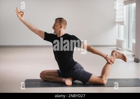 Un homme de construction athlétique fait du yoga dans la salle de gym sur un tapis. Banque D'Images