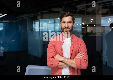 Portrait d'homme d'affaires prospère propriétaire de petite entreprise, homme mature dans une chemise rouge décontractée debout souriant et regardant l'appareil photo avec des bras croisés. Banque D'Images