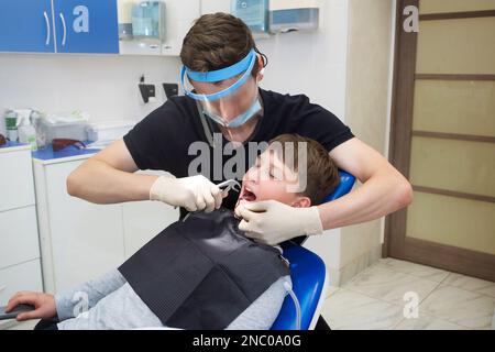 Un dentiste tirant une dent d'enfant avec des pinces dentaires Banque D'Images