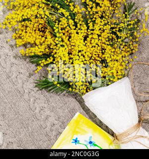 Bouquet de branches mimosa sur couverture tricotée avec photos d'enfants. Carte de vacances avec fleurs mimosa. Composition printanière adaptée à la fête des mères ou Banque D'Images
