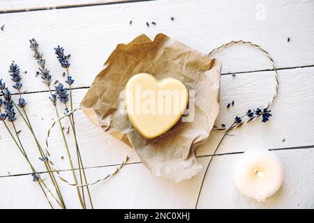 Cire d'abeille faite à la main et crème hydratante pour les mains au beurre de karité. Bar à crème en forme de coeur fait de tous les ingrédients naturels. Fond en bois blanc. Banque D'Images