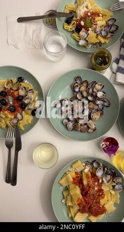 Un assortiment de délicieux plats italiens, notamment des pâtes et des palourdes servies avec un verre de vin rouge, pour une expérience culinaire parfaite Banque D'Images