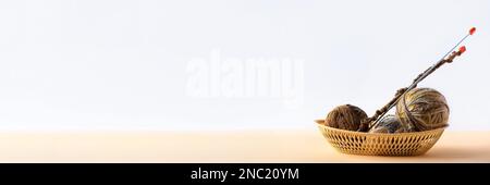 Boules de fil beige et marron dans un panier beige avec aiguilles à tricoter pour tricoter des vêtements chauds, tricoter hobby. Bannière Banque D'Images