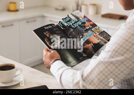 Homme avec café lisant le magazine sportif à table dans la cuisine, gros plan Banque D'Images