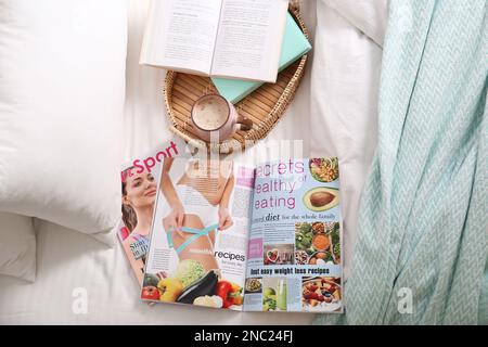 Différents magazines de style de vie, livres et café sur le lit, au-dessus de la vue Banque D'Images