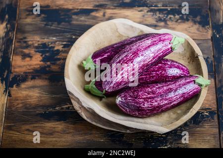 Aubergines de graffitis biologiques fraîches dans un bol en bois sur fond de béton. Banque D'Images