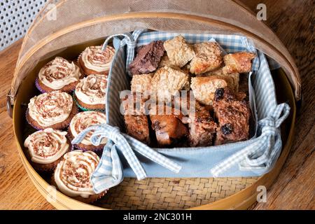 Un assortiment de gourmandises à gâteau, dont des gâteaux de tasse, des flapjacks et des tranches de pain Pudding. Tous sont présentés dans une couverture en bambou Banque D'Images